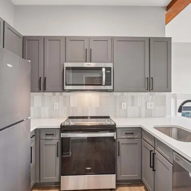 Modern Kitchen Design A modern kitchen featuring gray cabinetry, stainless steel appliances, and white countertops. The kitchen includes a built-in microwave, oven, and a sleek sink.