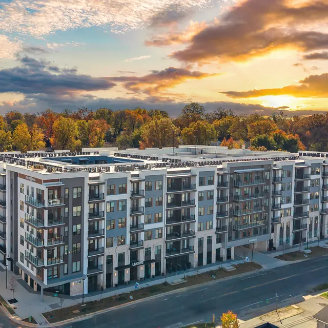Aerial view of a modern apartment building at sunset with colorful clouds and trees in the background.
