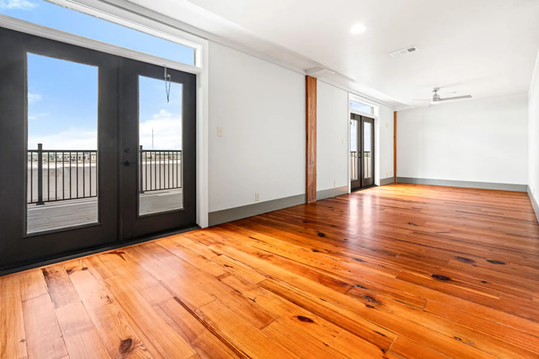 Bright interior of a modern apartment with hardwood floors and large glass doors leading to a balcony.