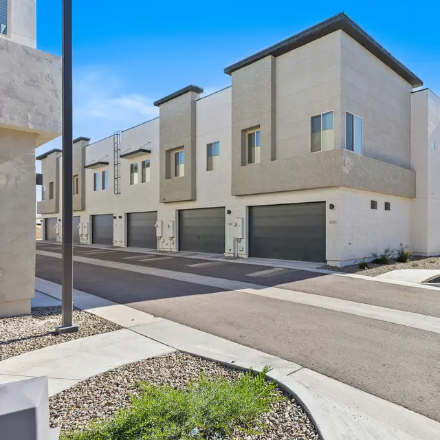 A view of modern townhouses with garages, featuring a clear blue sky and manicured landscaping.
