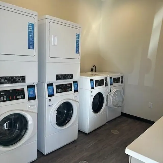 Modern Laundry Room Setup A modern laundry room featuring stacked washer and dryer units, alongside side-by-side washer and dryer machines, all in white. The room has a wooden floor with a beige wall and a bright light coming from the ceiling.