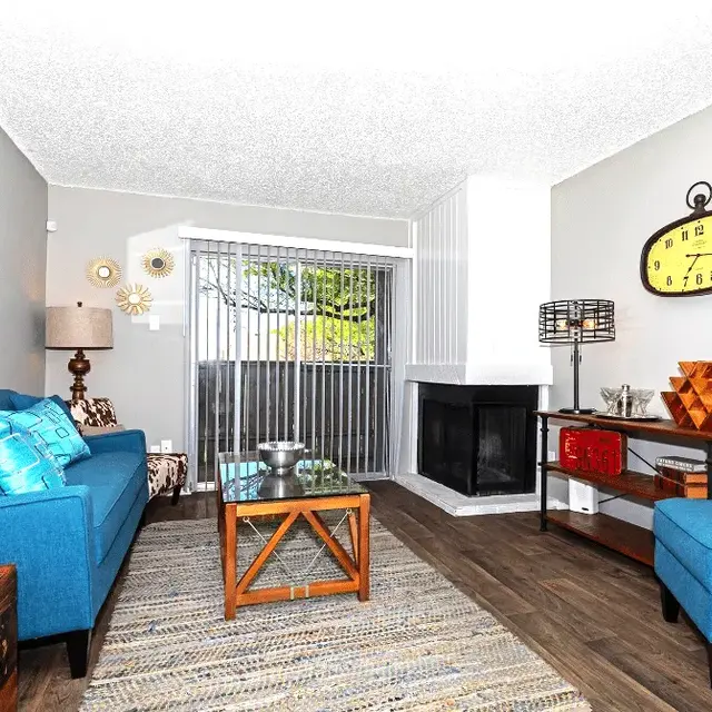 A cozy living room featuring blue sofas, a coffee table, a wall clock, and a decorative fireplace.