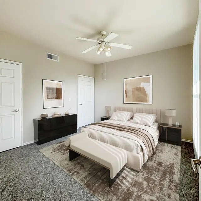 A modern and spacious bedroom featuring a bed with light bedding, two bedside tables, and a large area rug. The room has light-colored walls and a ceiling fan, with artwork hanging on the walls.