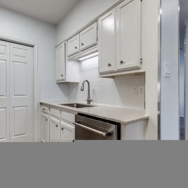 A modern kitchen featuring white cabinetry, a stainless steel refrigerator, and a sink with a faucet. The walls are painted in a light color, and the kitchen includes a countertop with an integrated dishwasher.