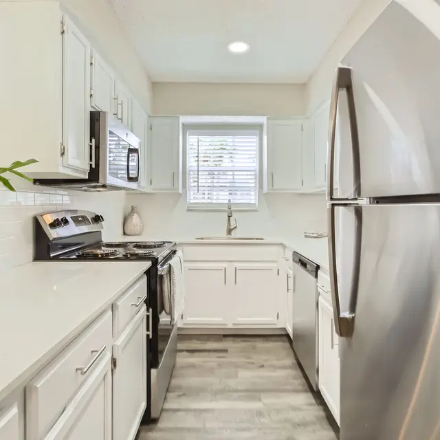 A contemporary kitchen featuring white cabinetry, stainless steel appliances, and a window with blinds.
