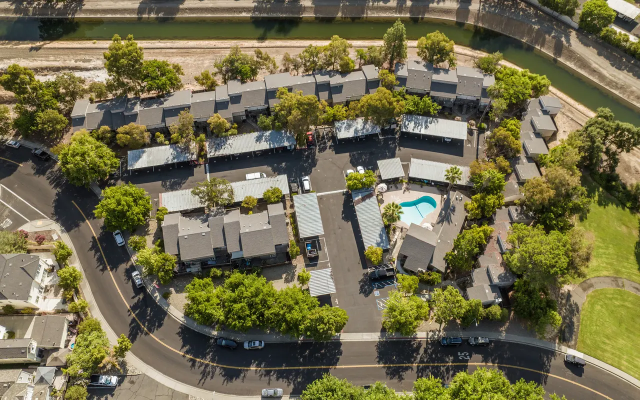 Aerial view of a hotel complex surrounded by greenery, featuring a swimming pool and a winding road.