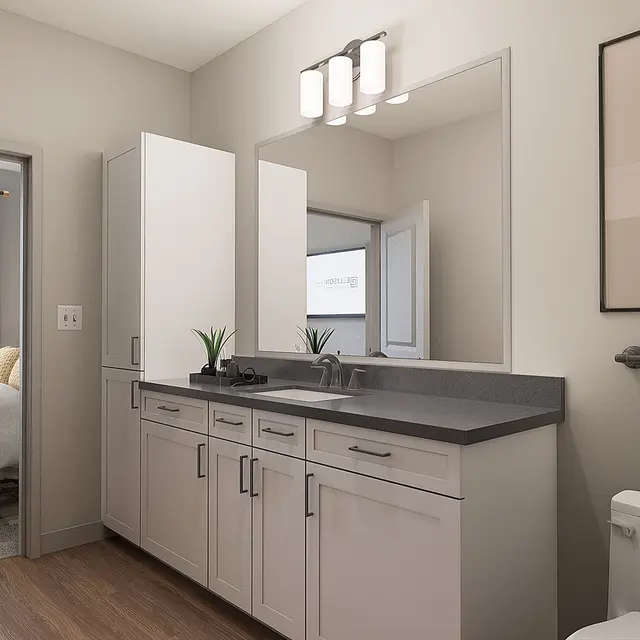 A bright, modern bathroom featuring a double sink vanity, large mirrors, and a gray countertop. There is also a wall-mounted towel rack with a patterned towel and a decorative print on the wall. The cabinetry is light-colored, and the floor is wooden.