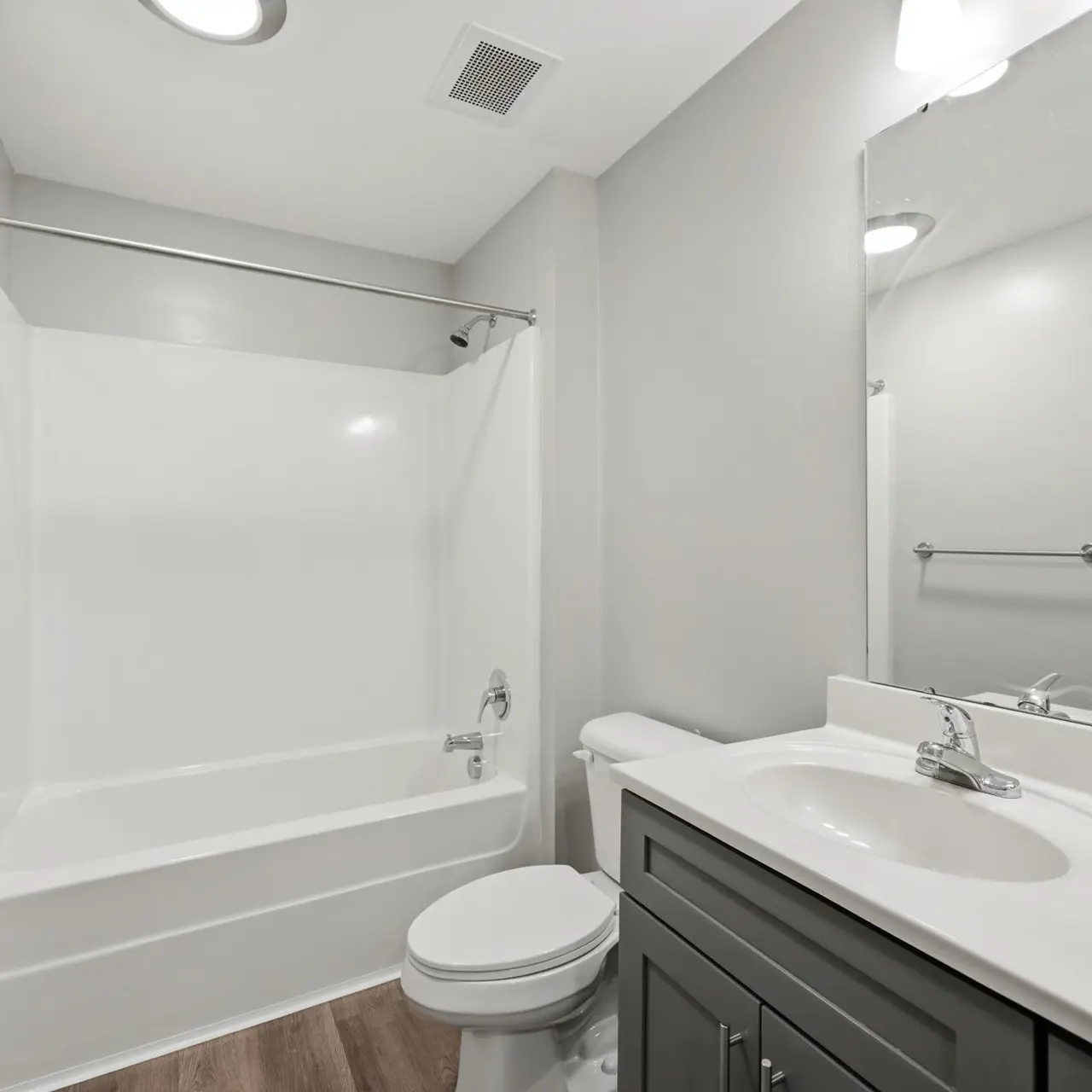 A clean and modern bathroom featuring a shower/tub combo, a white sink with a dark gray cabinet, and a large mirror above the sink.