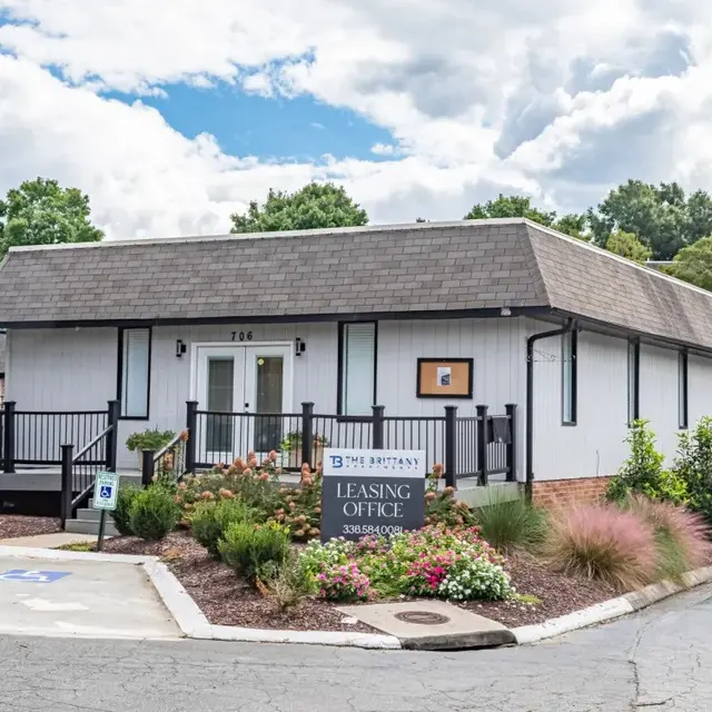 A modern leasing office building with a decorative landscape, featuring a porch and multiple entrance points.