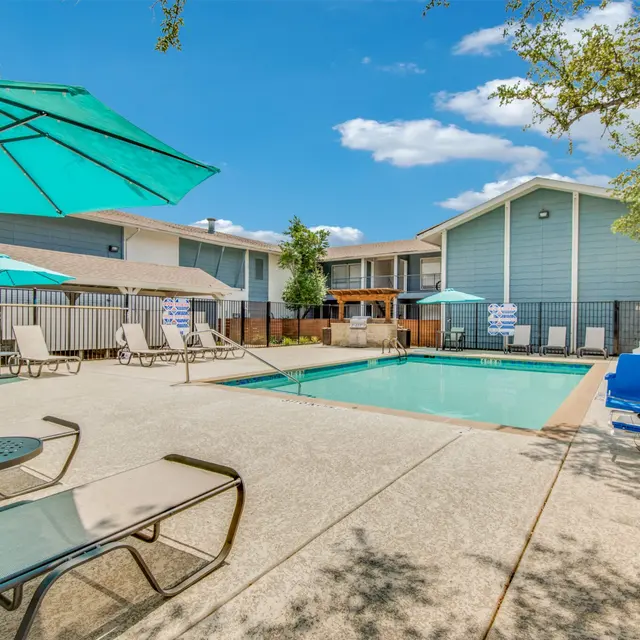 A swimming pool area with lounge chairs and umbrellas, surrounded by residential buildings.