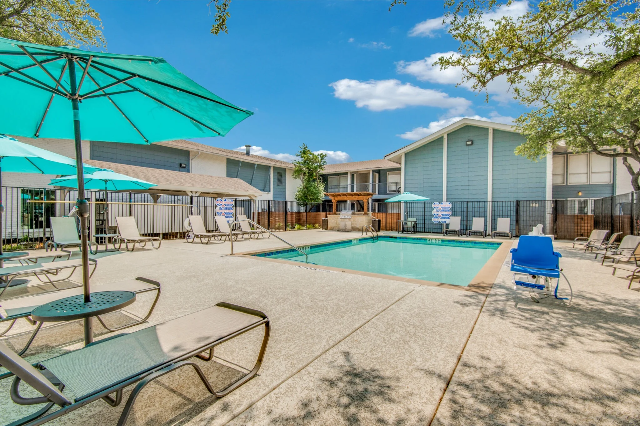 A swimming pool area with lounge chairs and umbrellas, surrounded by residential buildings.
