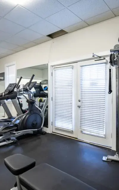 Interior view of a gym with exercise equipment, including treadmills, a weight machine, and large windows.