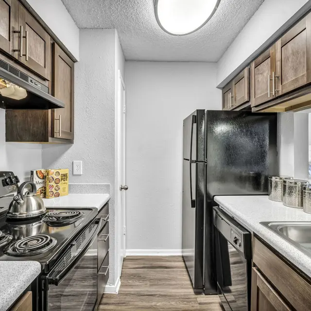 A modern kitchen with dark wooden cabinets, a stove, refrigerator, and stainless steel sink, featuring a clean, organized layout.