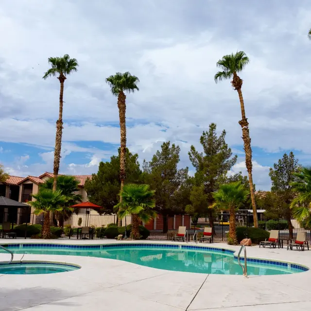 A serene pool area surrounded by palm trees and lounge chairs under a cloudy sky.