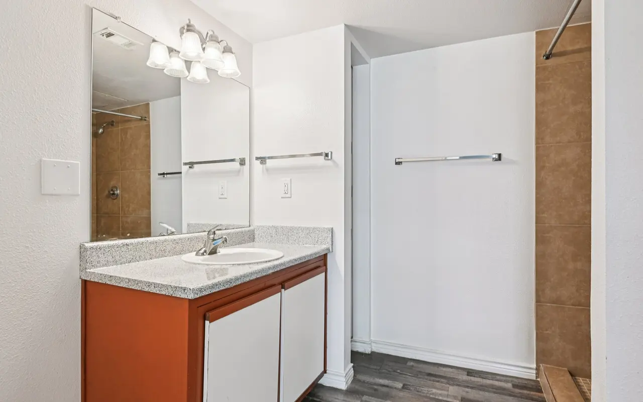 A modern bathroom featuring orange cabinetry, a white sink with a mirror above, and a spacious layout with tile flooring.