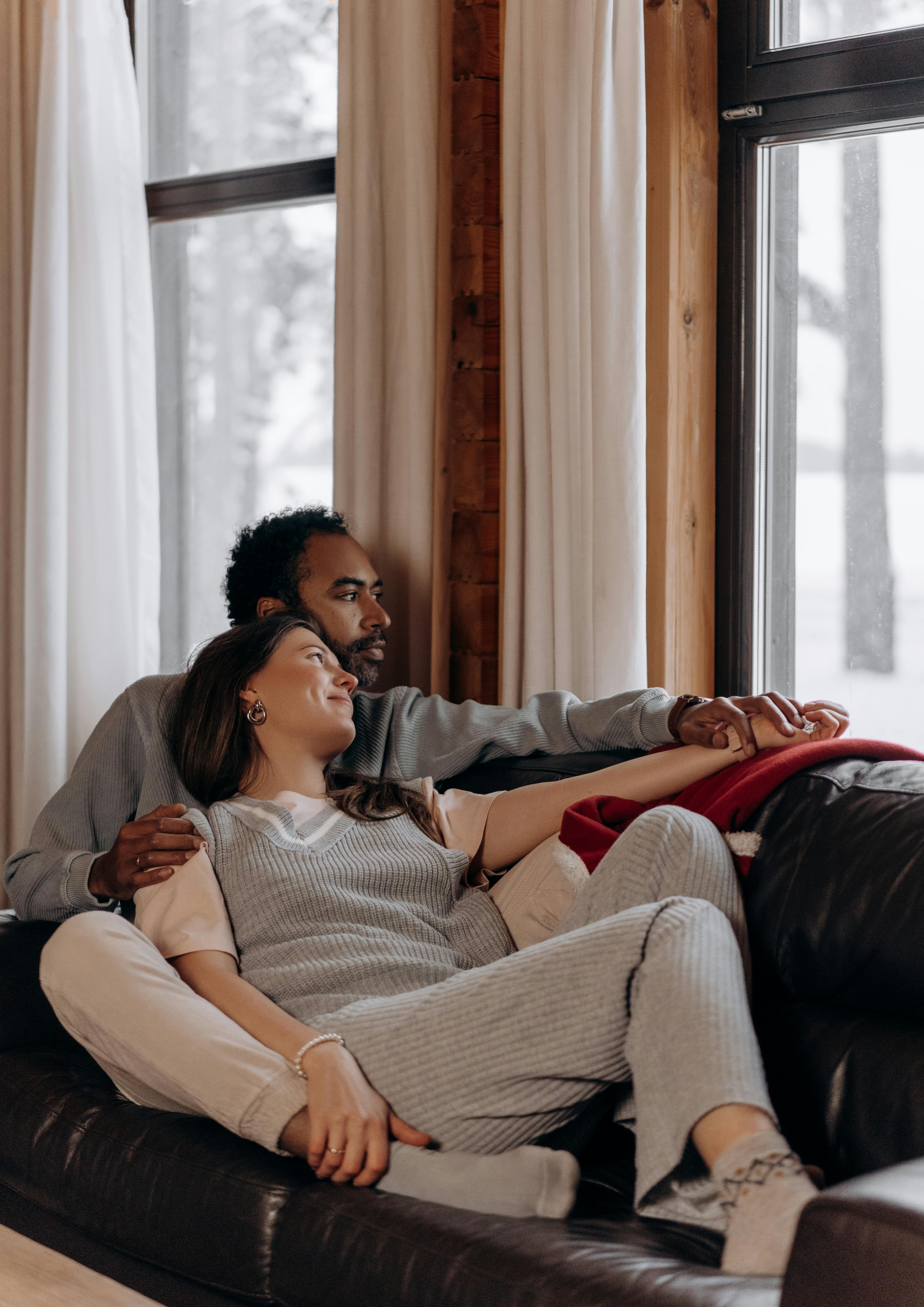Cozy Indoor Moments A couple sitting closely on a couch, gazing out of a window with snow outside.