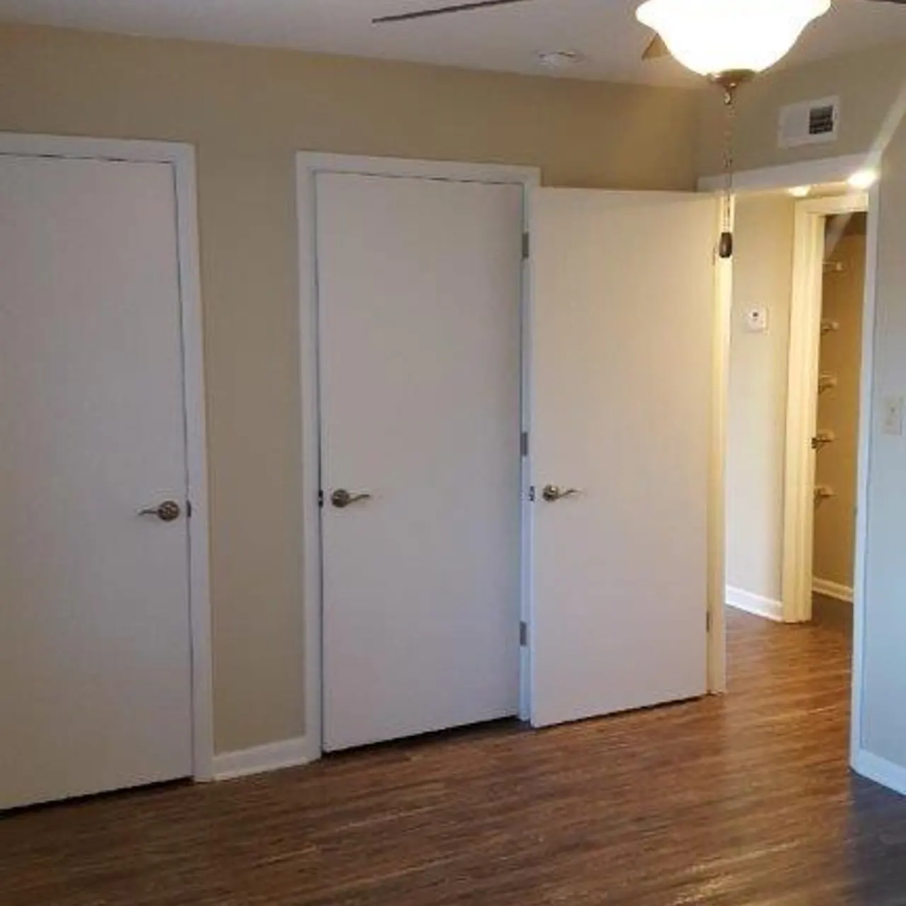 A room featuring three closed white doors on one wall, a ceiling fan above, and a view of another doorway in the background.