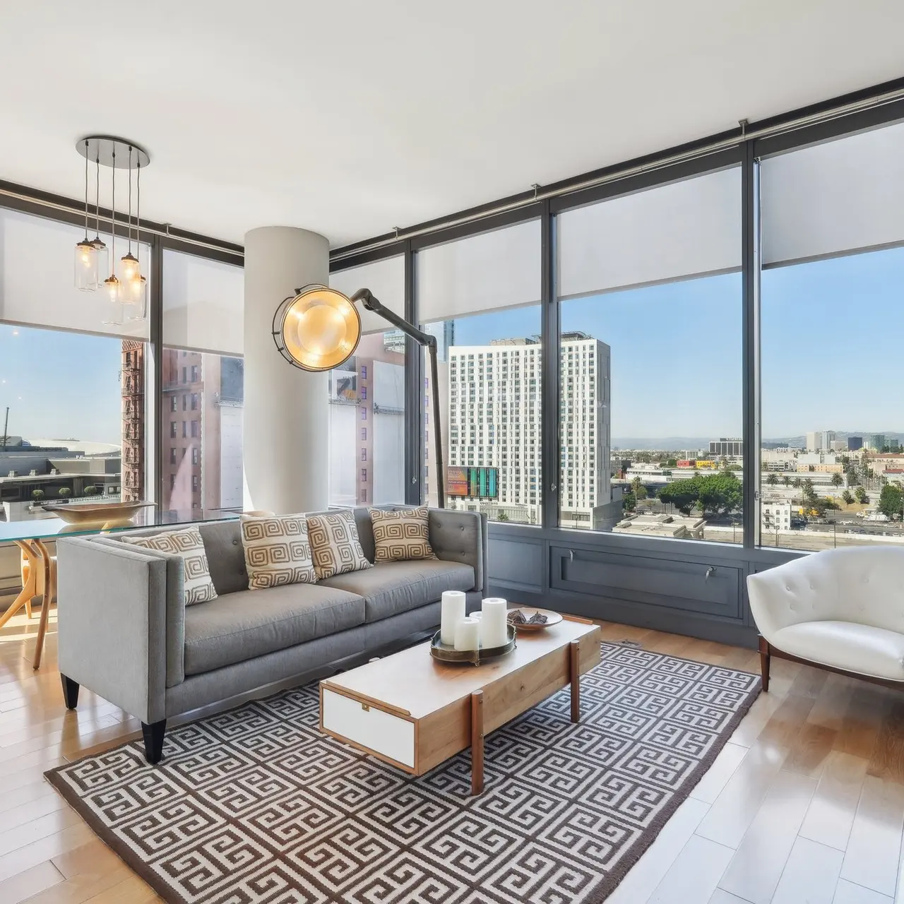 A stylish modern living room featuring large windows with city views, a gray sofa, and a coffee table on a geometric-patterned rug.