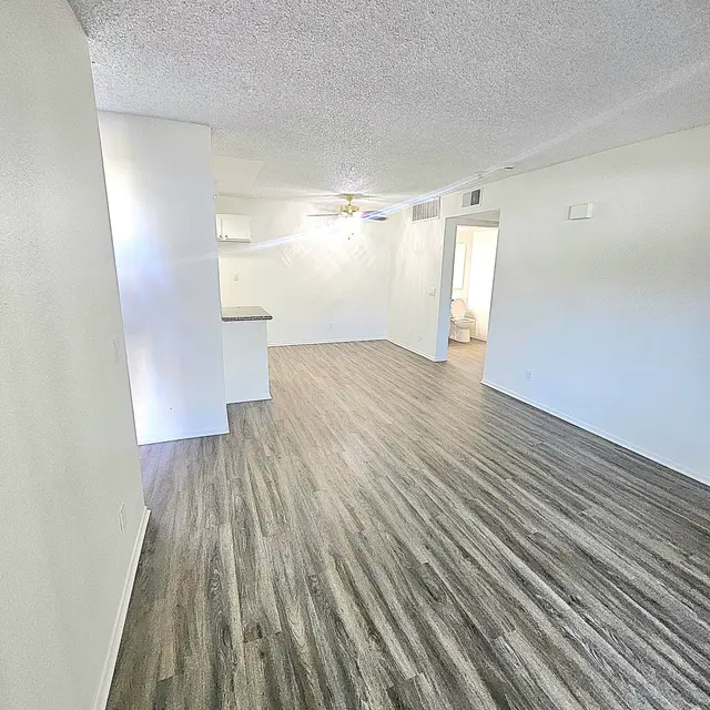 Spacious living area of a modern apartment with light-colored walls and wooden flooring.