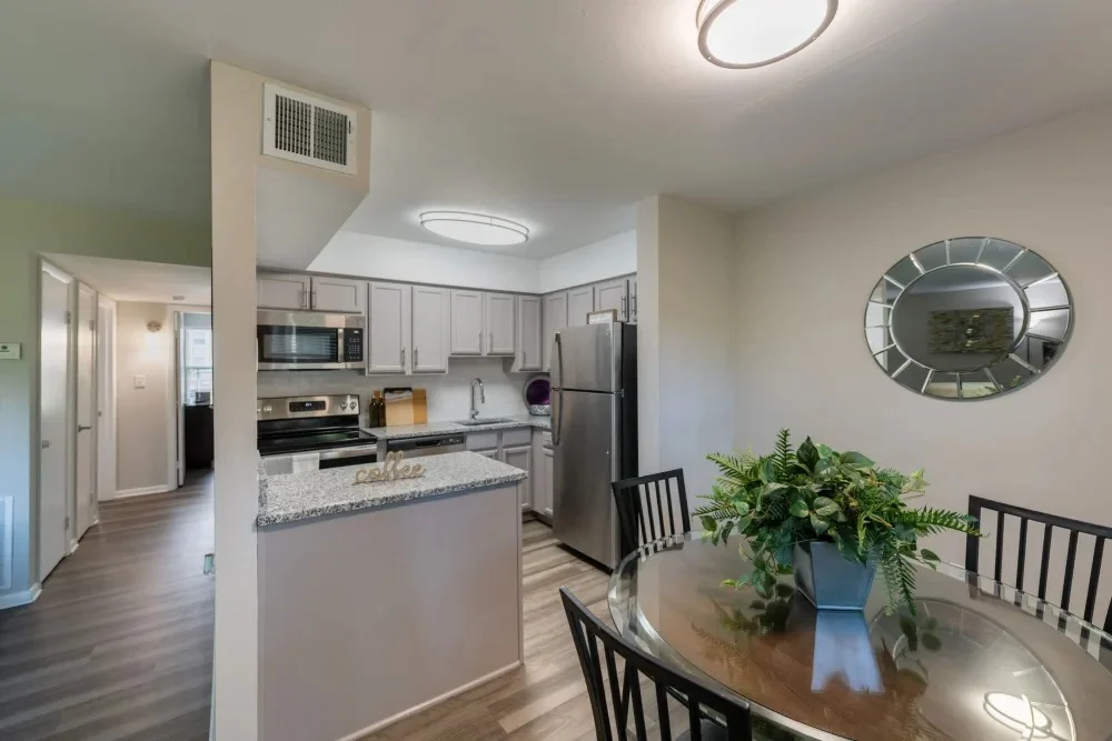 A modern kitchen and dining area featuring stainless steel appliances, a round dining table with black chairs, and a mirrored wall decoration.