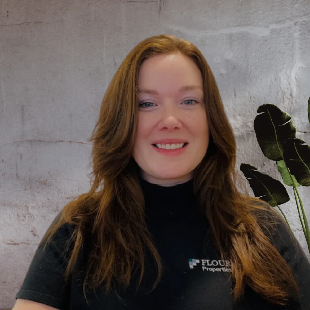A smiling woman with long hair wearing a black shirt in front of a light textured background.