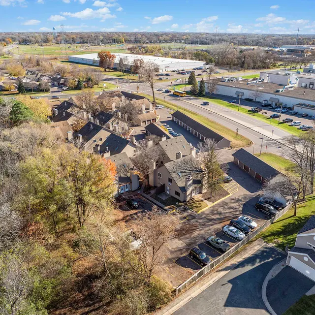 Aerial view of a residential area with trees and a parking lot, surrounded by roads and commercial buildings.