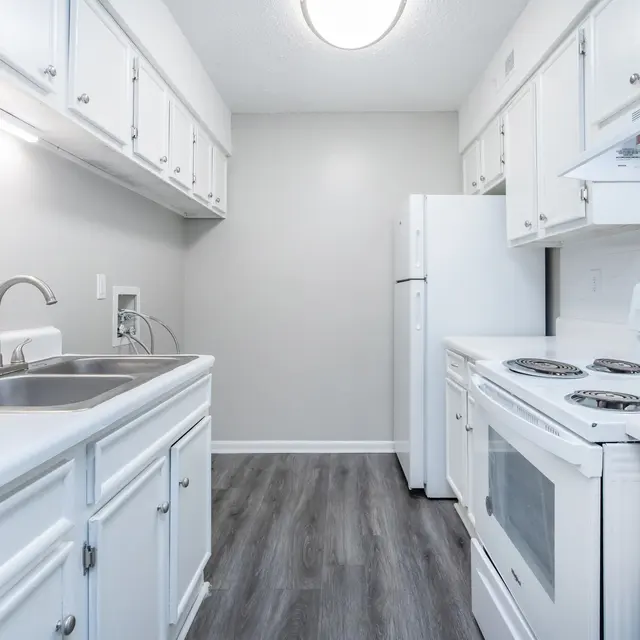 A modern kitchen with white cabinetry, a stainless steel sink, and appliances including a refrigerator and stove.