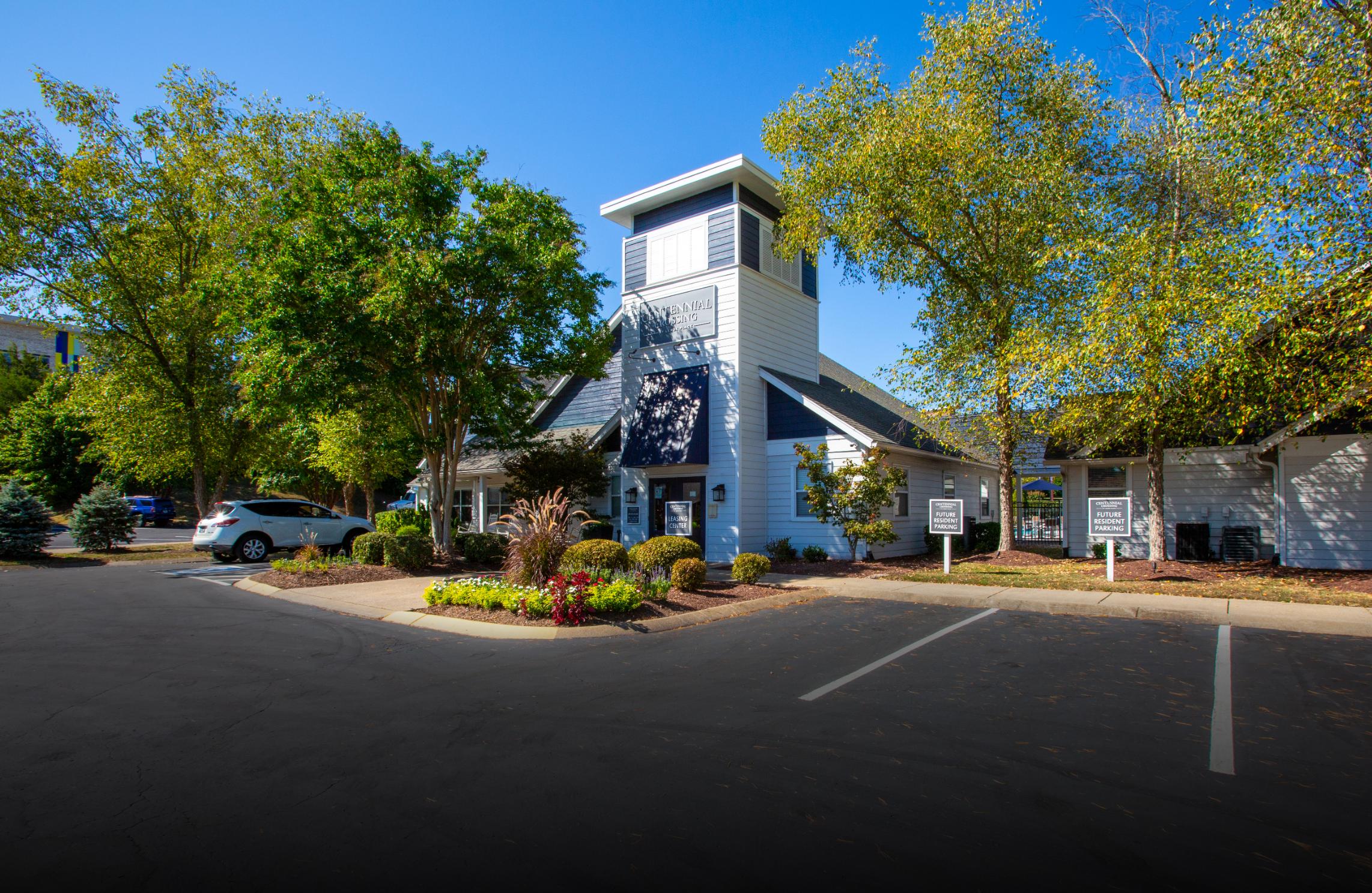 A well-maintained building with a tower, surrounded by lush greenery and a parking area on a sunny day.