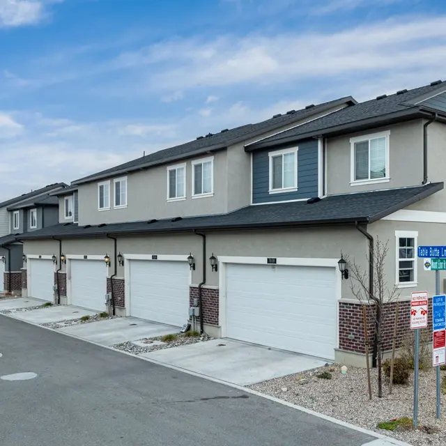 A row of modern townhomes with garages along a paved street, under a cloudy sky.
