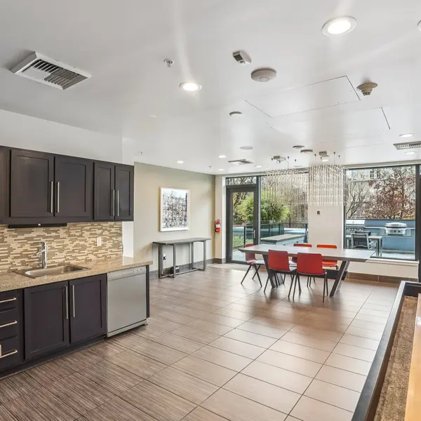 A modern kitchen with dark cabinetry and a dining area featuring red chairs and large windows that overlook an outdoor space.