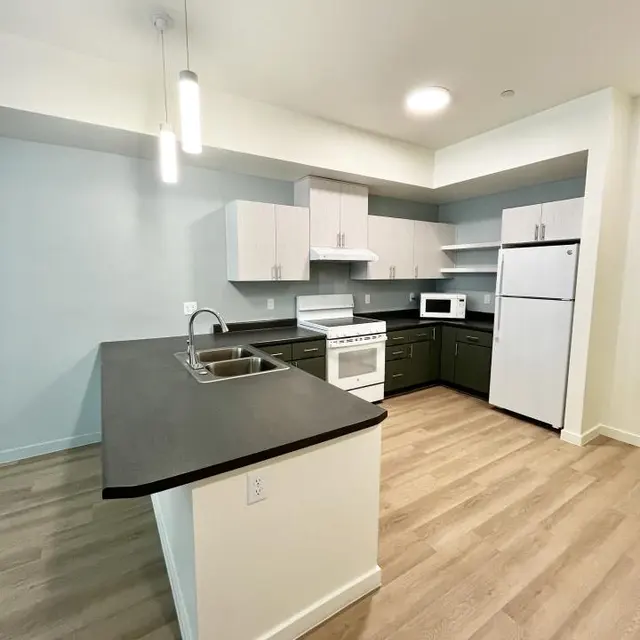 A modern kitchen featuring a central island with a sink, a range and microwave in a compact layout, and light-colored cabinets with a hint of pale blue walls.