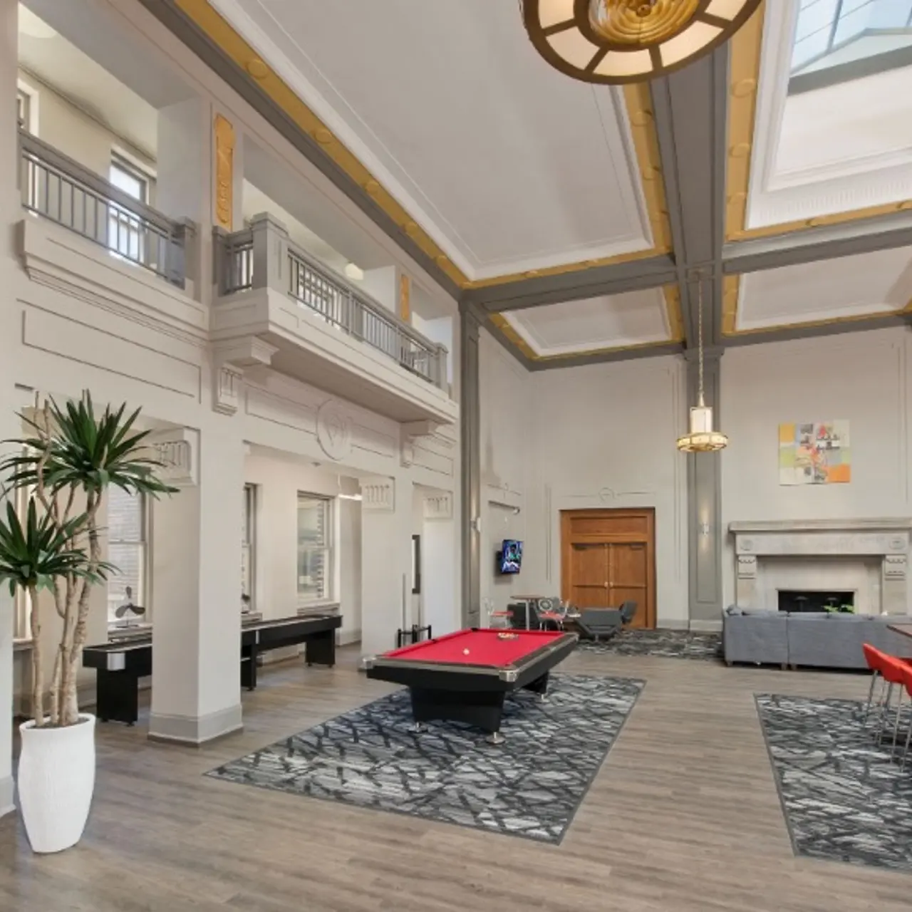 A spacious modern living area featuring a pool table, dining table, and a decorative fireplace. Large windows let in natural light, and plants add greenery to the space.