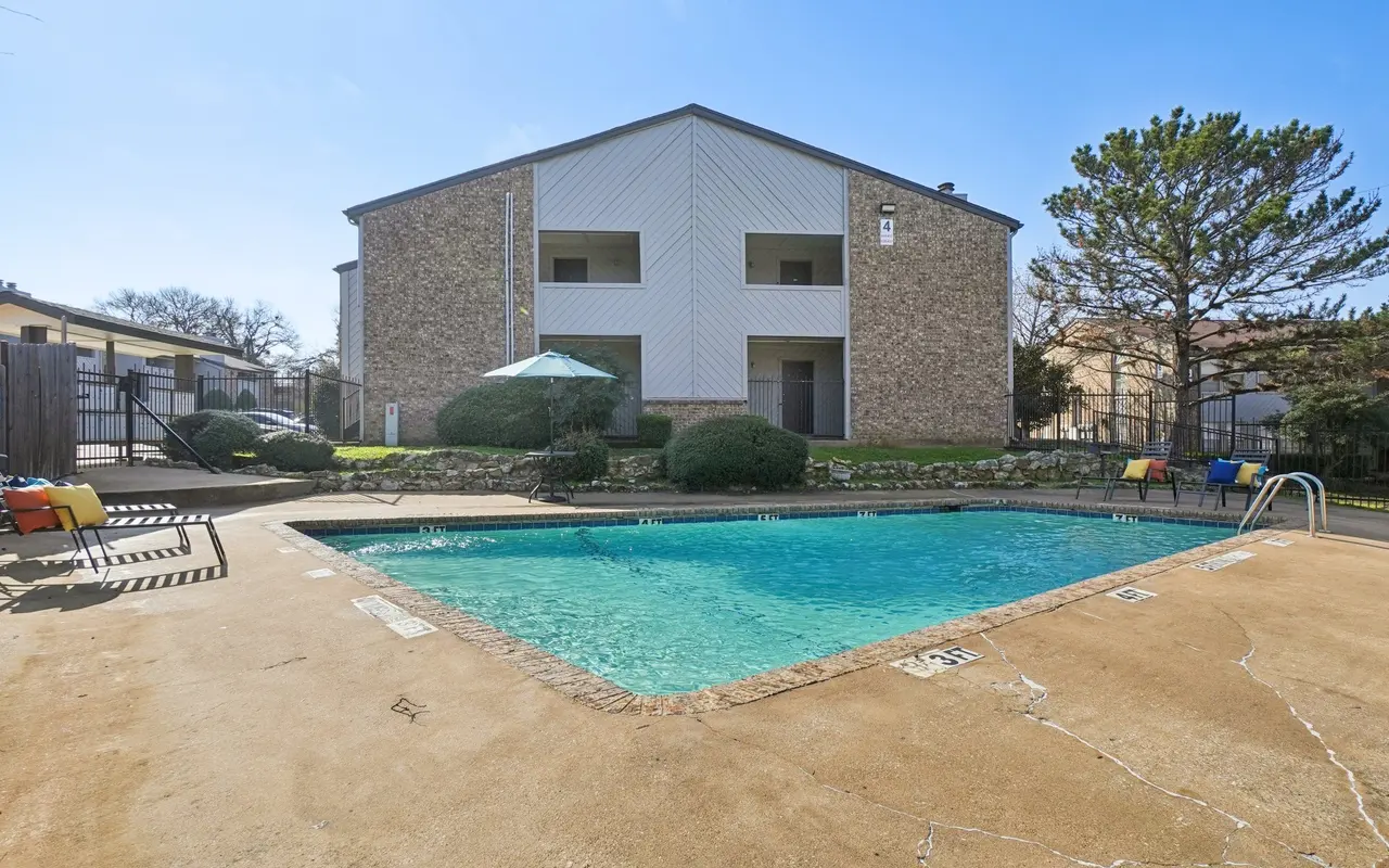 Outdoor swimming pool at an apartment complex with lounge chairs and an umbrella.