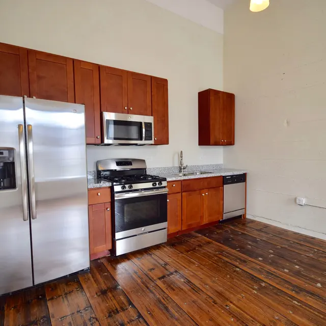 A modern kitchen featuring stainless steel appliances, wooden cabinets, and a rustic wooden floor.