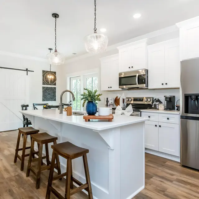 Modern kitchen featuring white cabinetry, stainless steel appliances, a large island with bar stools, and pendant lighting.