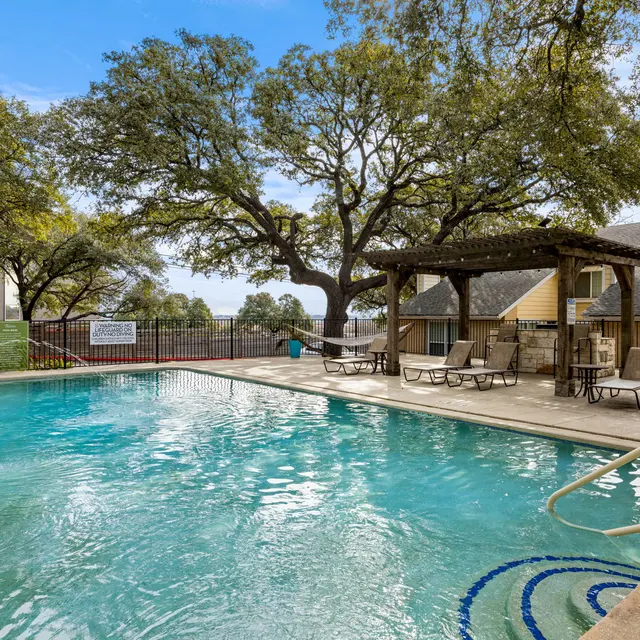 A serene pool area surrounded by trees with lounge chairs on the deck.