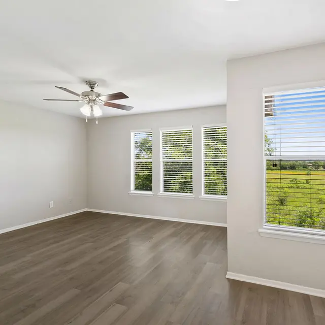 Spacious Empty Room with Scenic View A spacious, empty room with a ceiling fan and large windows showing a scenic view of greenery outside.