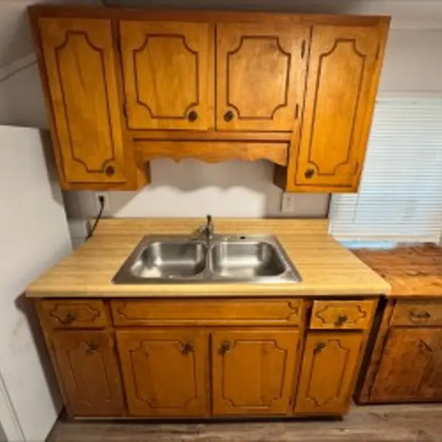 A small kitchen area featuring wooden cabinets, a double sink, and a countertop.
