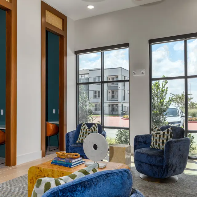 A modern and stylish lounge area with blue chairs, wooden accents, and large windows letting in natural light, showcasing an outdoor view.