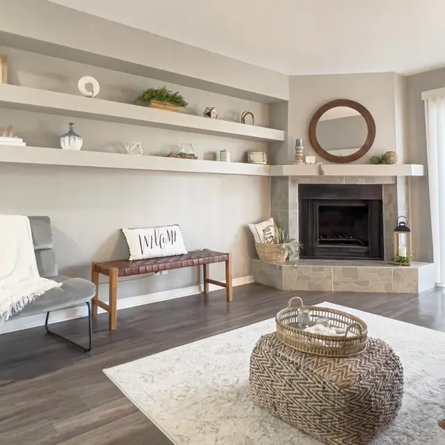 Cozy living room featuring a fireplace, shelves with decor, a woven ottoman, and a light rug, creating a welcoming atmosphere.