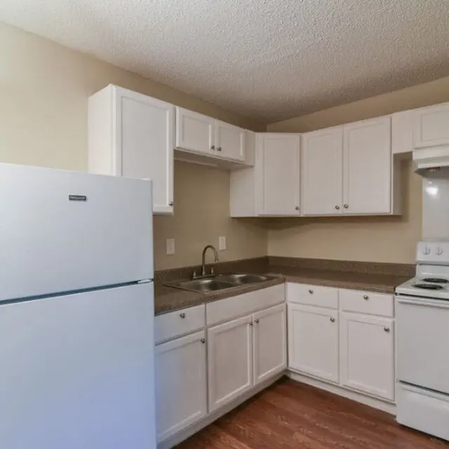 A small kitchen featuring white cabinets, a white refrigerator, a sink, and a white stove with a hood.