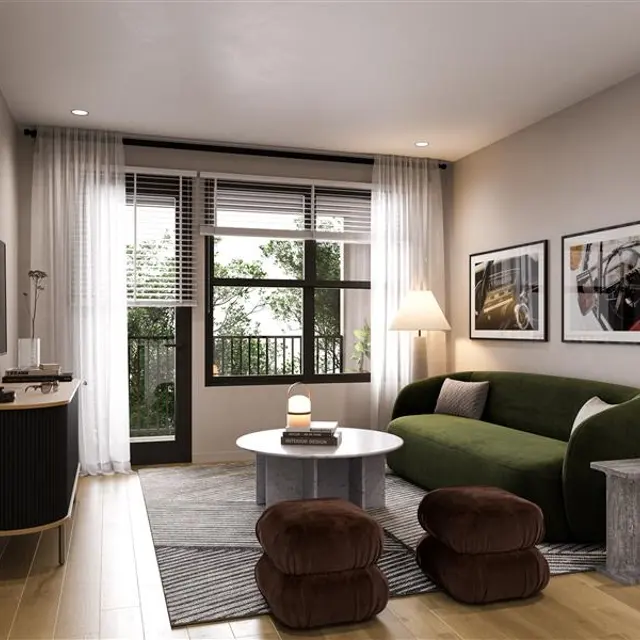 A modern living room featuring a green sofa, a round coffee table, and two poufs. There are large windows with curtains, art on the walls, and a TV on a console.