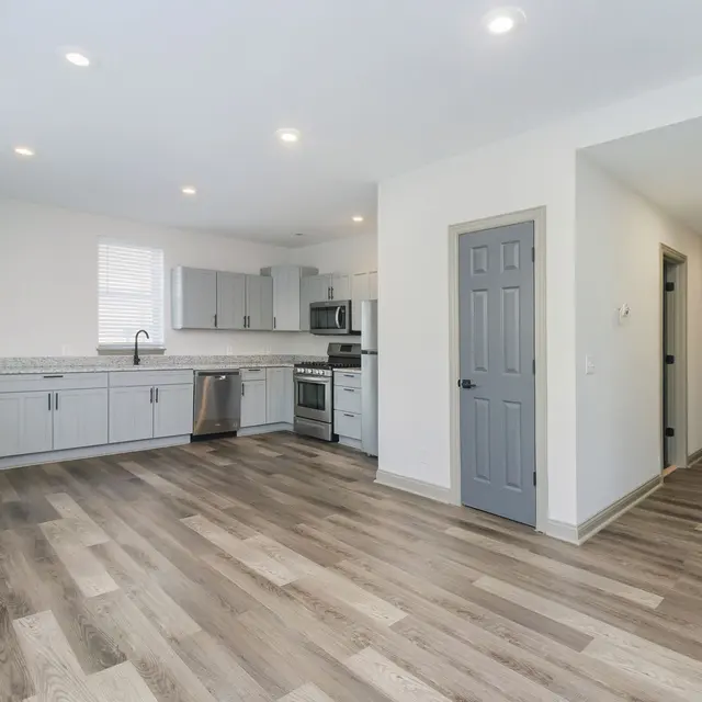 A modern kitchen and living area featuring gray cabinets, stainless steel appliances, and a light-colored floor.