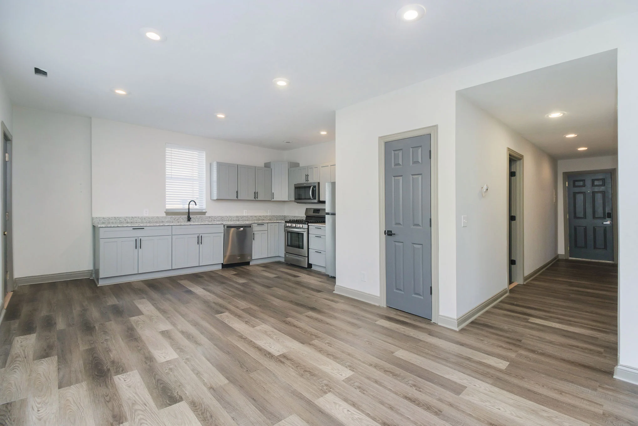 A modern kitchen and living area featuring gray cabinets, stainless steel appliances, and a light-colored floor.