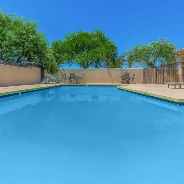 Relaxing Swimming Pool Area A clear and inviting swimming pool surrounded by a patio with chairs and trees in the background, under a bright blue sky.