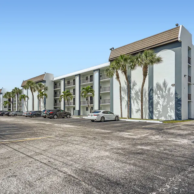 View of a multistory apartment building surrounded by palm trees and parking spaces.