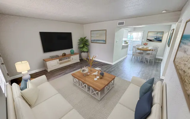 Cozy Modern Living Room A modern living room featuring a white sectional sofa, a light wood coffee table, and a large television mounted on the wall. There are decorative items on the table and a green plant in the corner. The room has neutral-colored walls and flooring, leading to a dining area in the background.