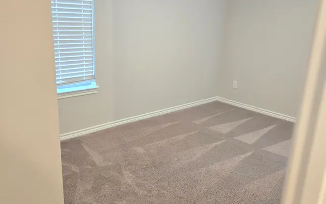 Empty Bedroom with Natural Light An empty bedroom featuring light gray walls and new carpet. A window with blinds on the left side allows natural light to enter. The ceiling has a fan giving a modern touch. There are no furnishings in the room, creating a spacious feel.