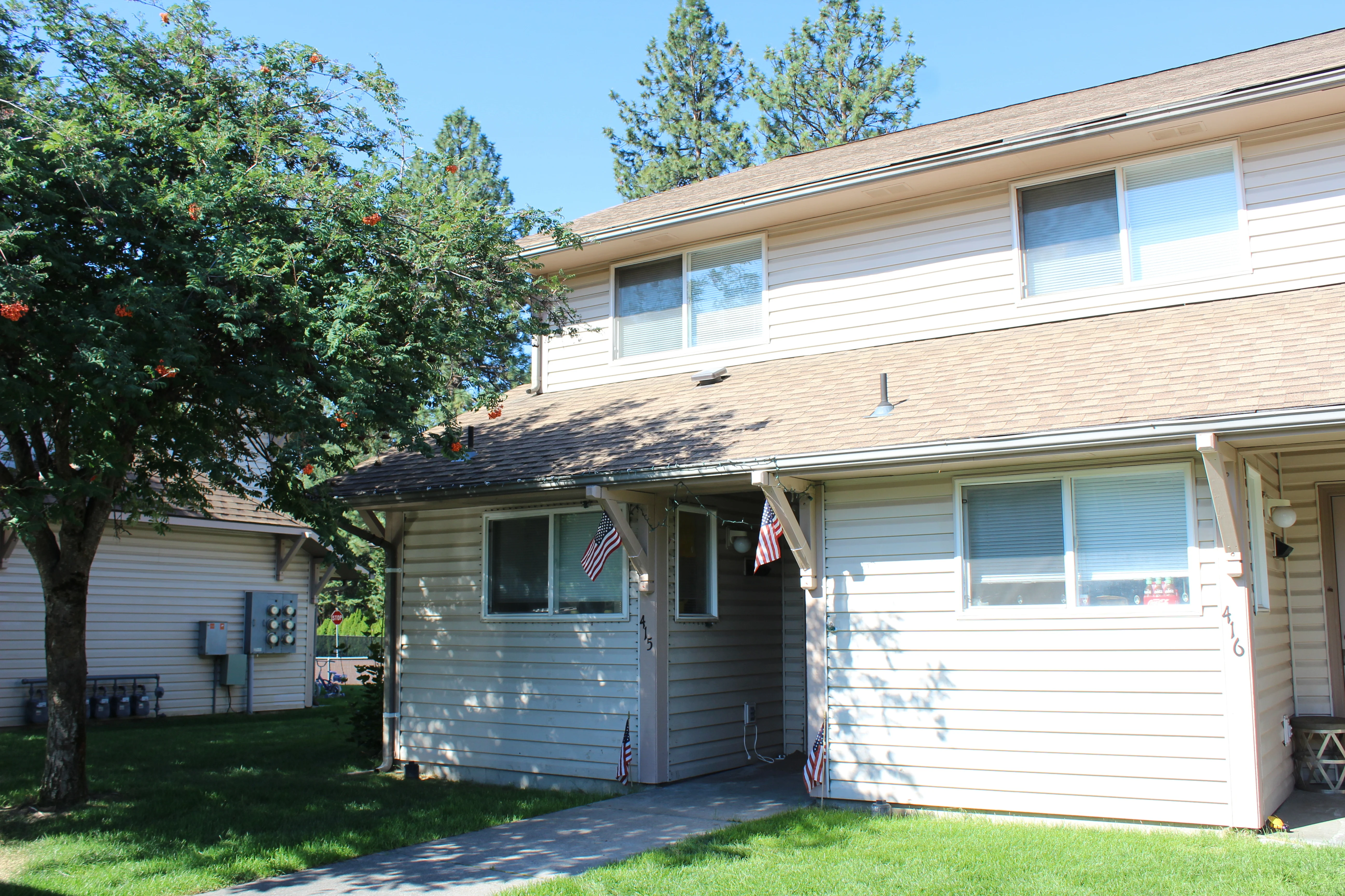 Exterior view of a two-story apartment building with green lawn and trees