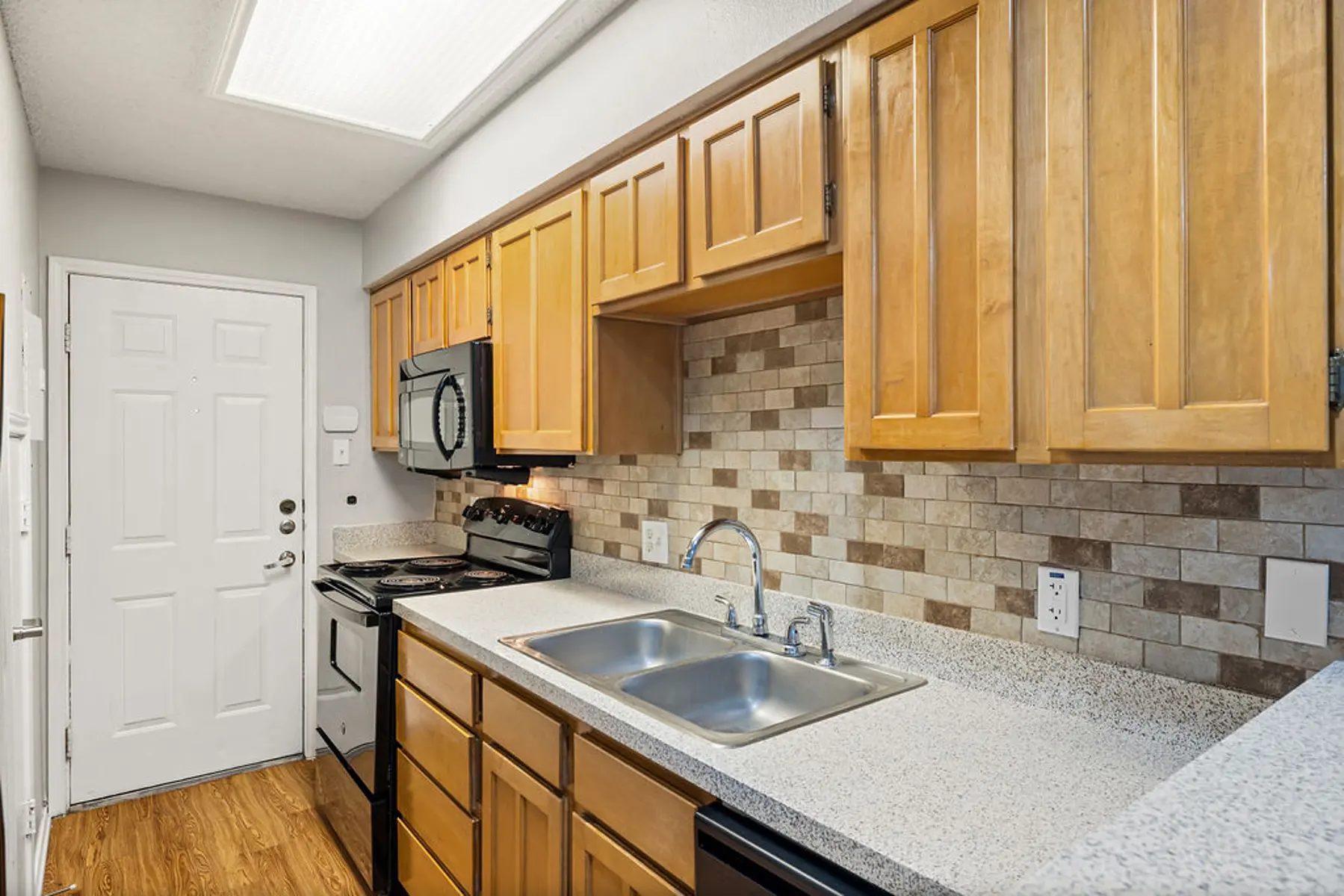 Modern Kitchen Design A modern kitchen featuring wooden cabinets, a double sink, a stove, and a tiled backsplash. A door is visible on the left side.